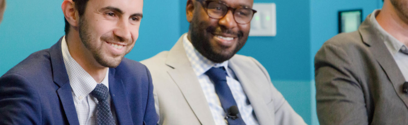 two men sitting next to each other in suits, smiling