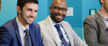 two men sitting next to each other in suits, smiling