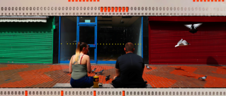 Two people sat facing shuttered high street shops.