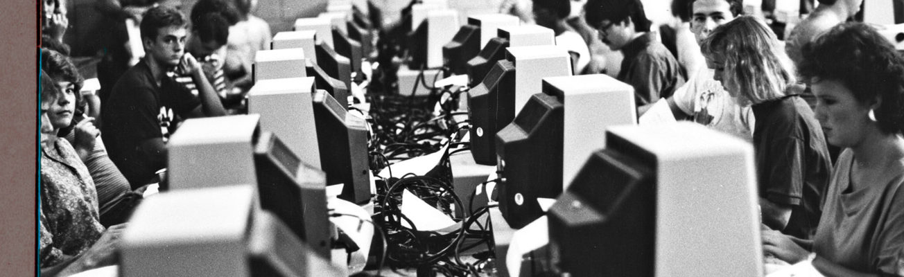 A black and white photograph of people sitting at a bank of computers