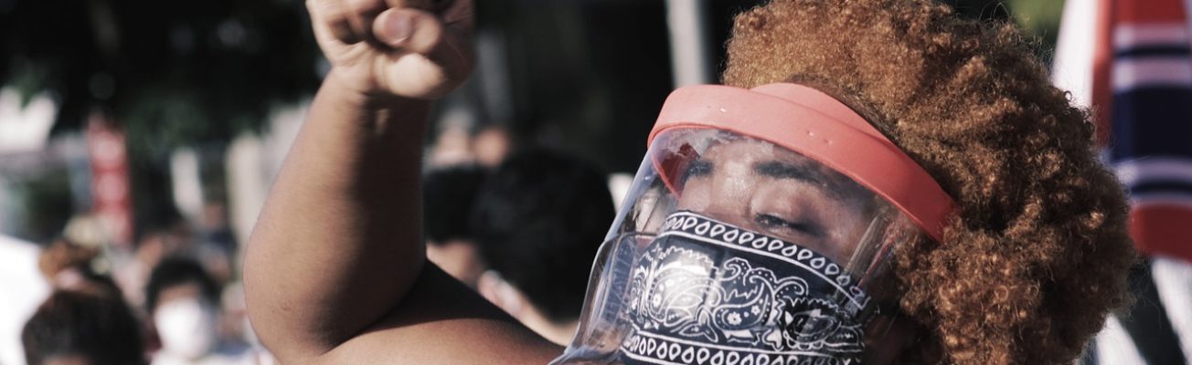 a protester in Brazil wags their finger while wearing a bandana and face visor