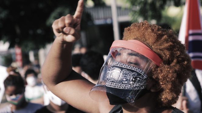 a protester in Brazil wags their finger while wearing a bandana and face visor