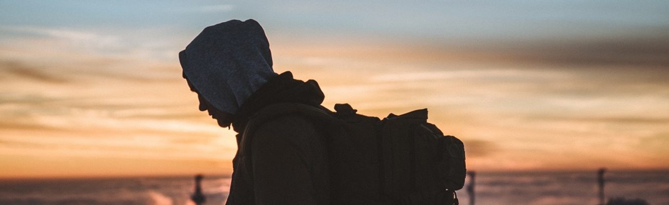boy wearing hoodie and rucksack lit against a sunset