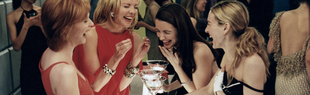 The four protagonists of sex and the city stand in a cocktail bar laughing