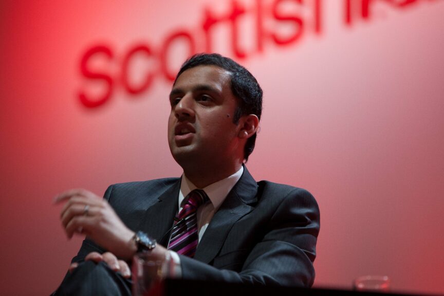 Scottish Labour leader Anas Sarwar sitting cross-legged in front of a sign that reads 'Scottish Labour'