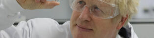 Prime minister Boris Johnson in a white labcoat and protective goggles, holding up a vial of the coronavirus vaccine