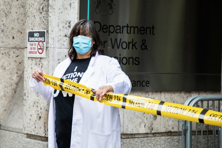 Activist and artist Dolly Sen holds yellow tape across the front of the DWP offices, to "section" the department