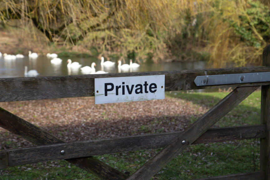 A "private" sign on a wooden gate with swans in a lake behind it