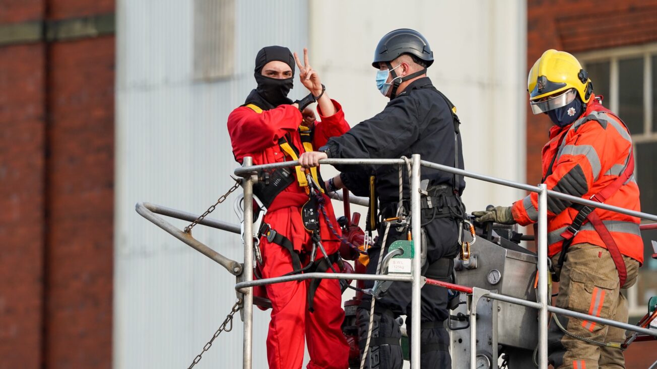 A protester gives a V finger sign while being handcuffed by workers on a crane