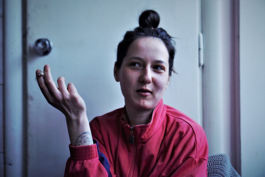 A woman with dark brown hair in a top knot and a red tshirt holds one hand up towards her face