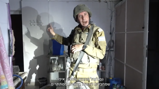 an israeli soldier with mouth agape stands in front of a spotlight, pointing at something behind him