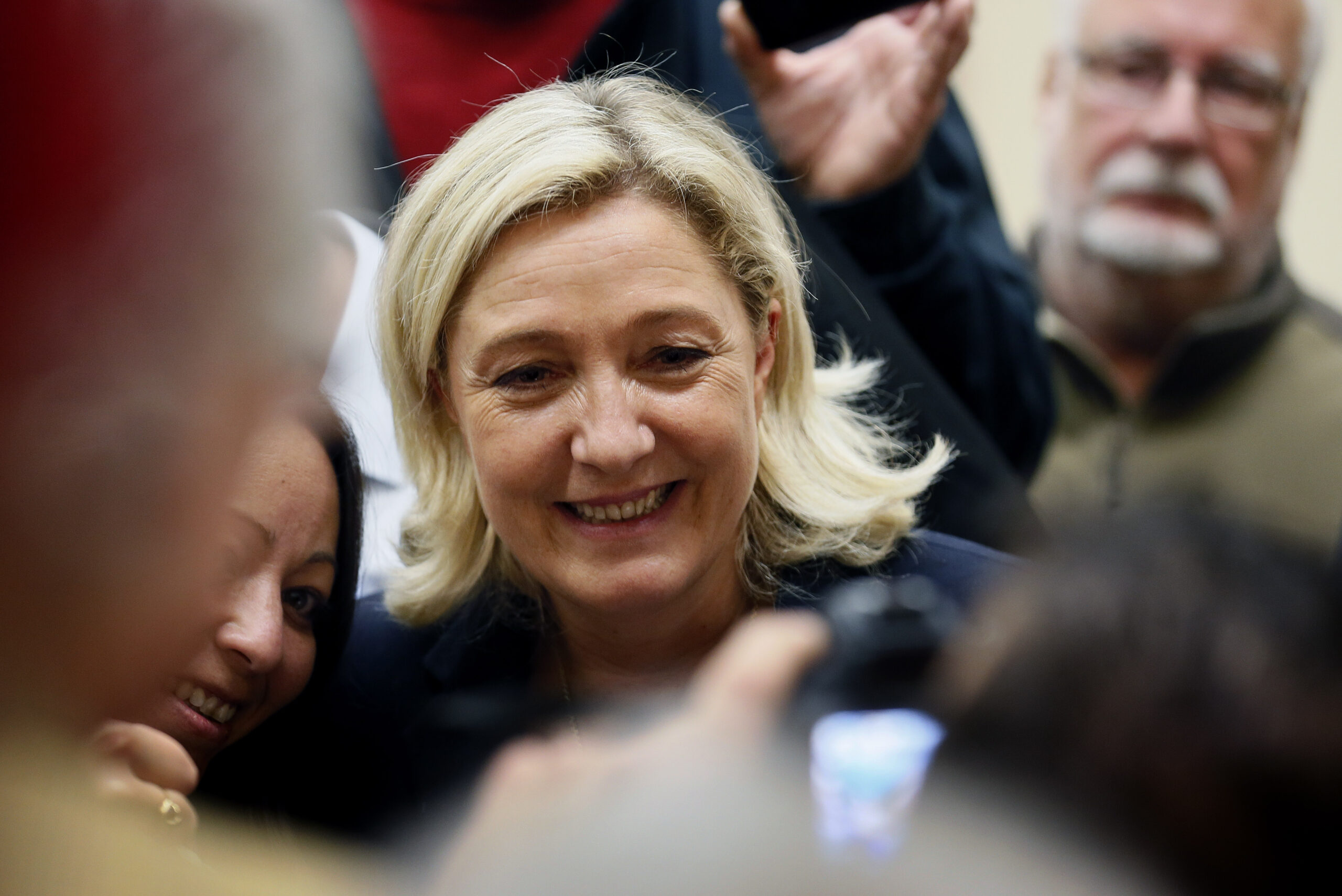 A woman with blonde bobbed hair smiles as she passes through a crowd