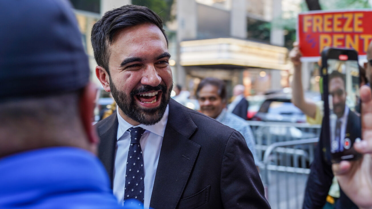A man smiles in foreground with a sign saying 'freeze the rent' in the background