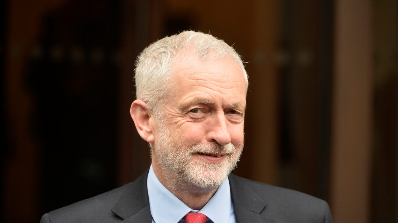 A man with white hair and red tie smiles at the camera