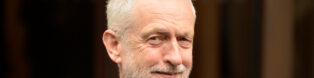 A man with white hair and red tie smiles at the camera