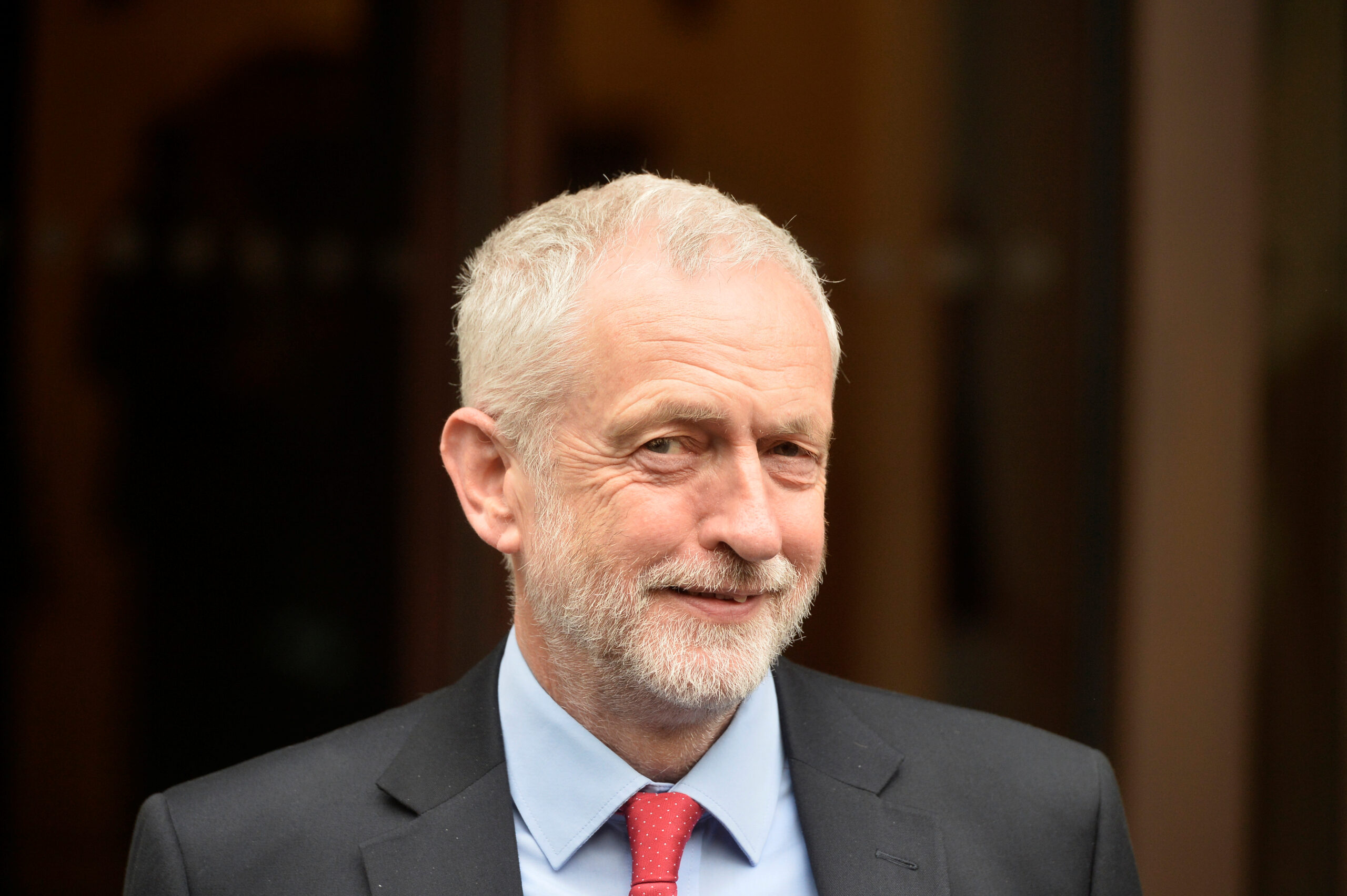 A man with white hair and red tie smiles at the camera