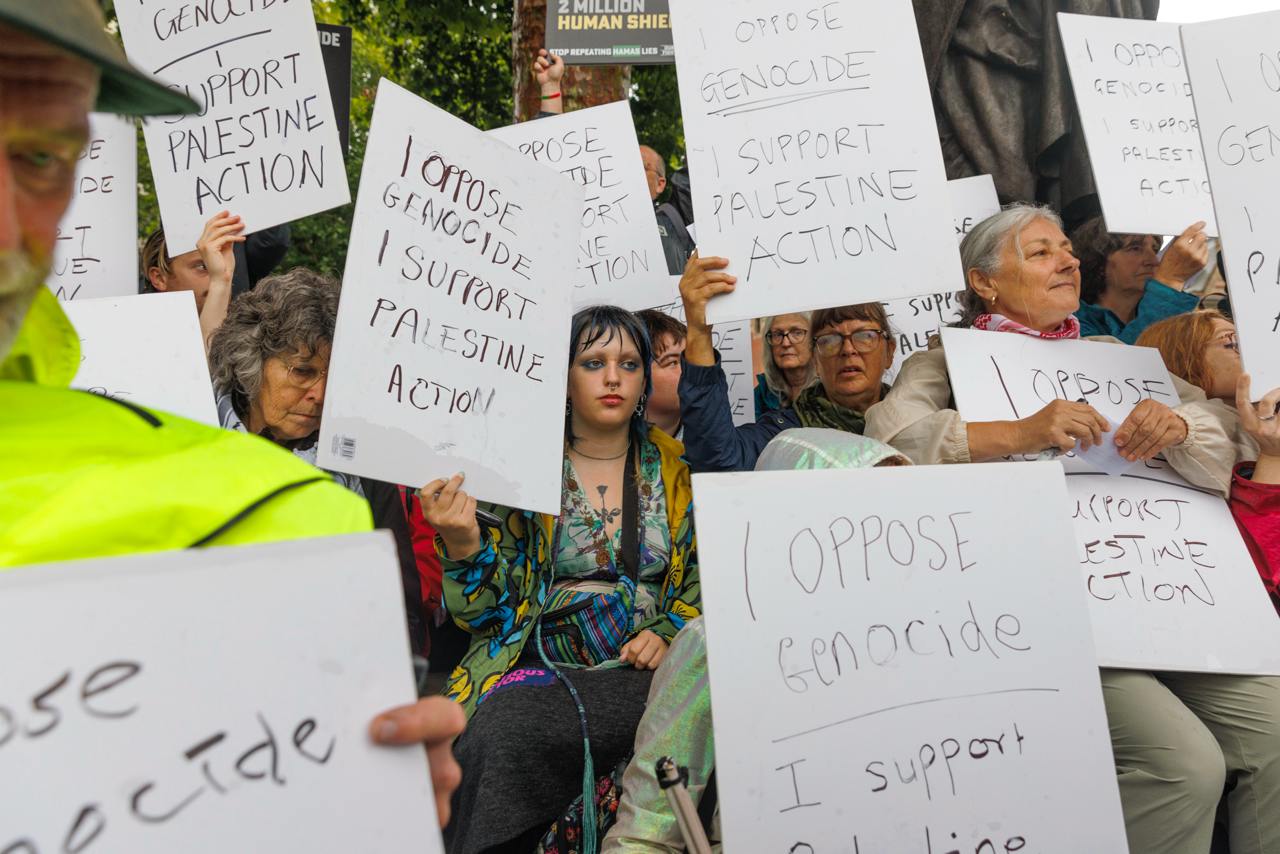 Protests sit quietly holding signs that say "I oppose genocide. I support Palestine Action."