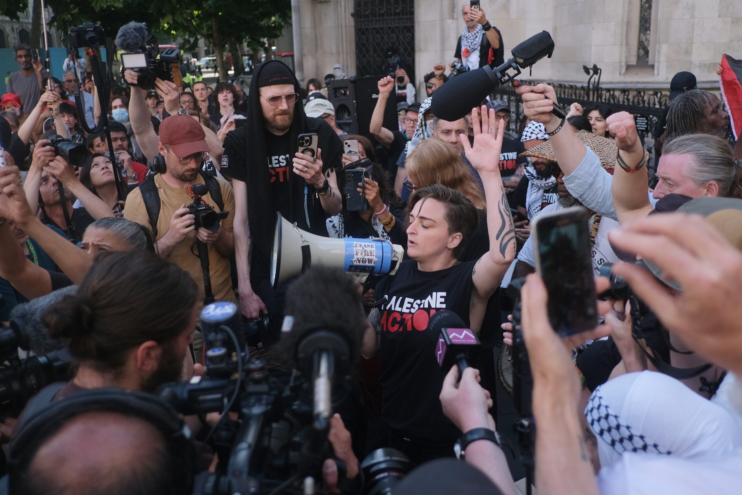 A person raises their hand in the air on a loudhailer as a press pack gathers around them