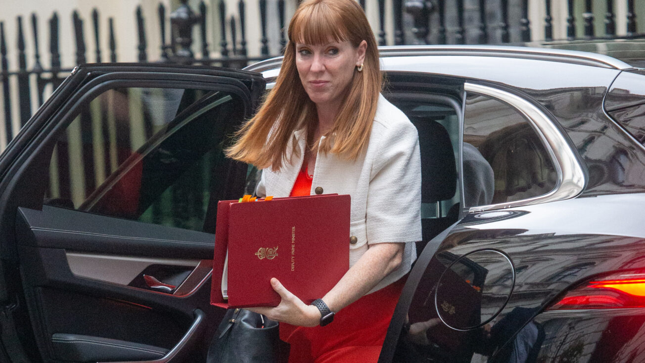A woman with long red hair steps out of a cab carrying a red briefcase
