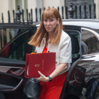 A woman with long red hair steps out of a cab carrying a red briefcase