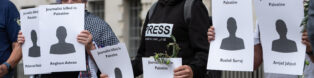 A person with a black hoodie that says 'press' on it holds a piece of card that has a cut-out figure with the words 'journalist killed in palestine', and the name of a killed Gazan journalist.
