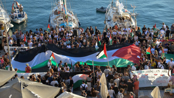 A Palestinian flag is seen as people gather at the port of Ermoupolis before the departure of two sailing boats, Electra and Oxygen, part of the Global Sumud Flotilla aiming to reach Gaza and break Israel's naval blockade, on Syros island, Greece, September 14, 2025