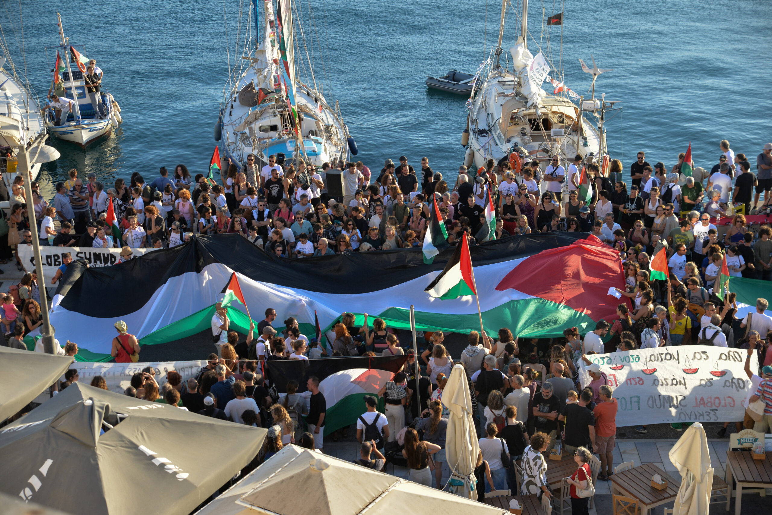 A Palestinian flag is seen as people gather at the port of Ermoupolis before the departure of two sailing boats, Electra and Oxygen, part of the Global Sumud Flotilla aiming to reach Gaza and break Israel's naval blockade, on Syros island, Greece, September 14, 2025