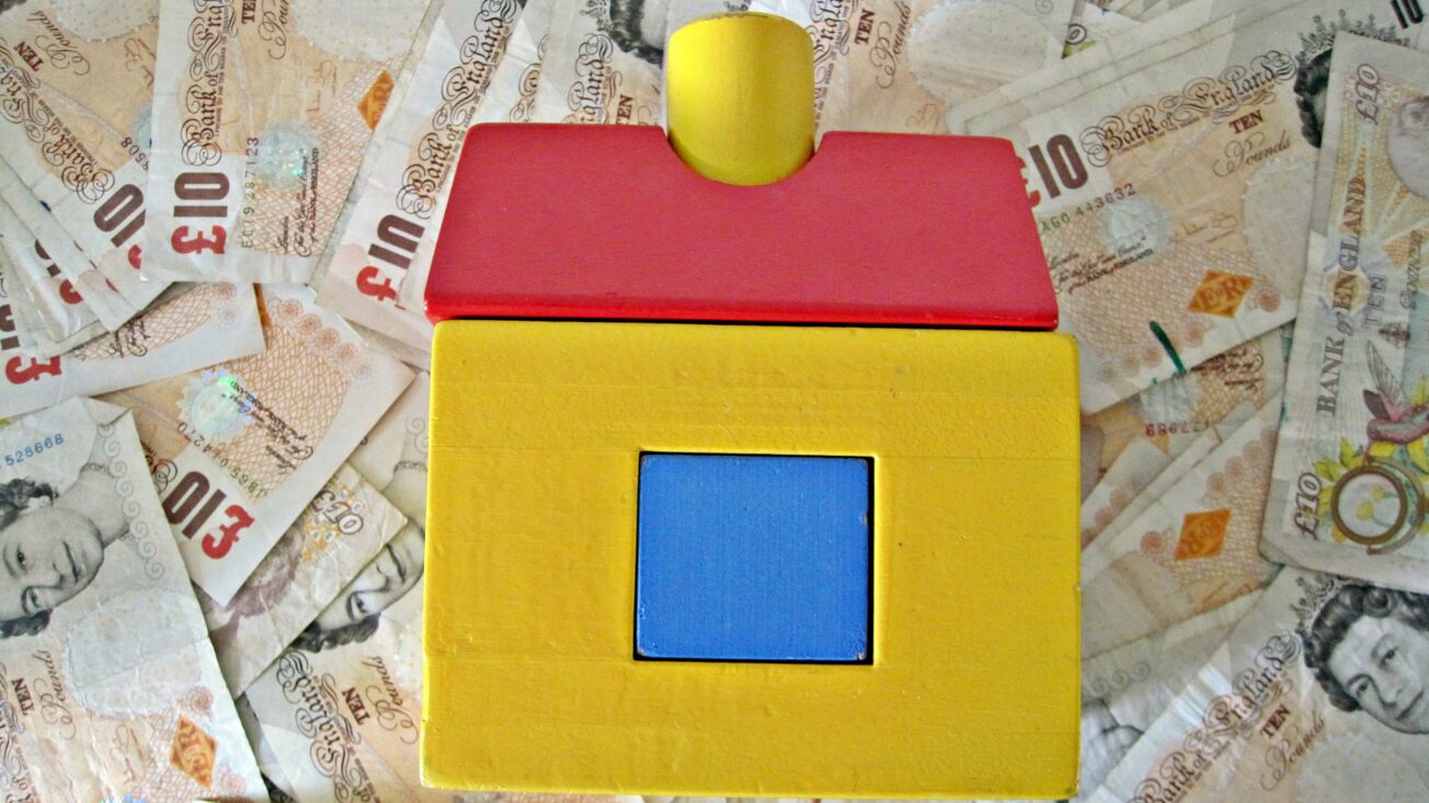 a wooden house toy on top of a pile of £10 notes