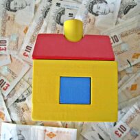 a wooden house toy on top of a pile of £10 notes