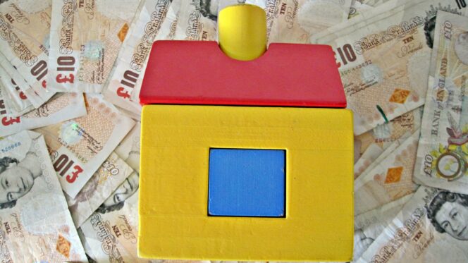 a wooden house toy on top of a pile of £10 notes