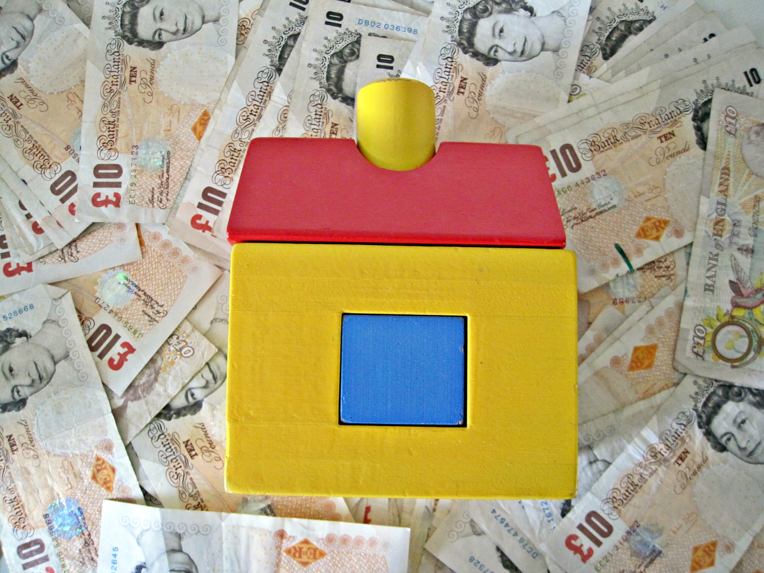 a wooden house toy on top of a pile of £10 notes