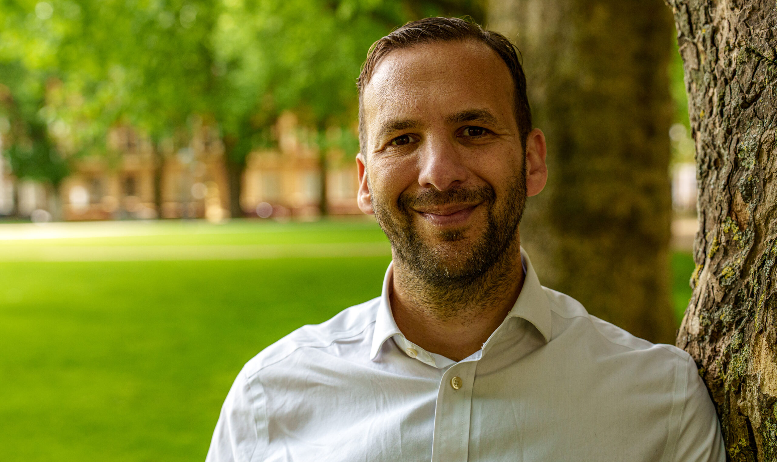a man in a white shirt with stubble smiles at the camera