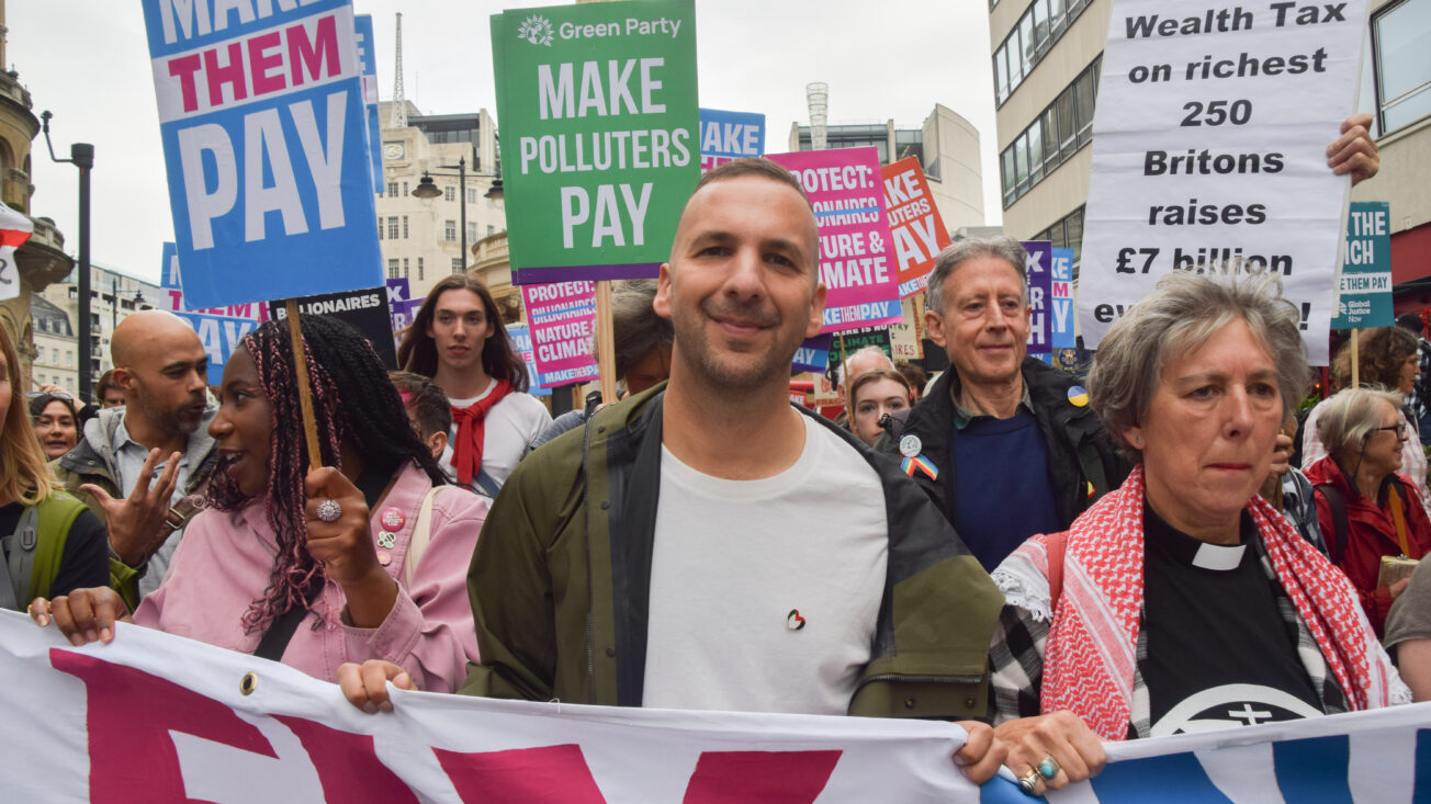A man in a green jacket and white t-shirt holds a banner alongside other activists