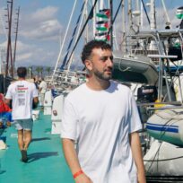 Kieran Andrieu walks down a pier past boats flying Palestine flags.