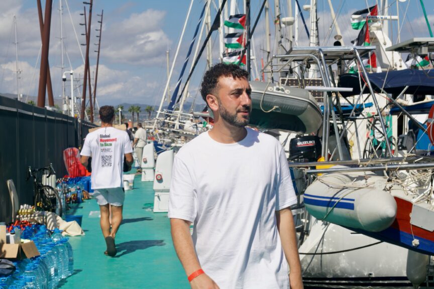 Kieran Andrieu walks down a pier past boats flying Palestine flags.