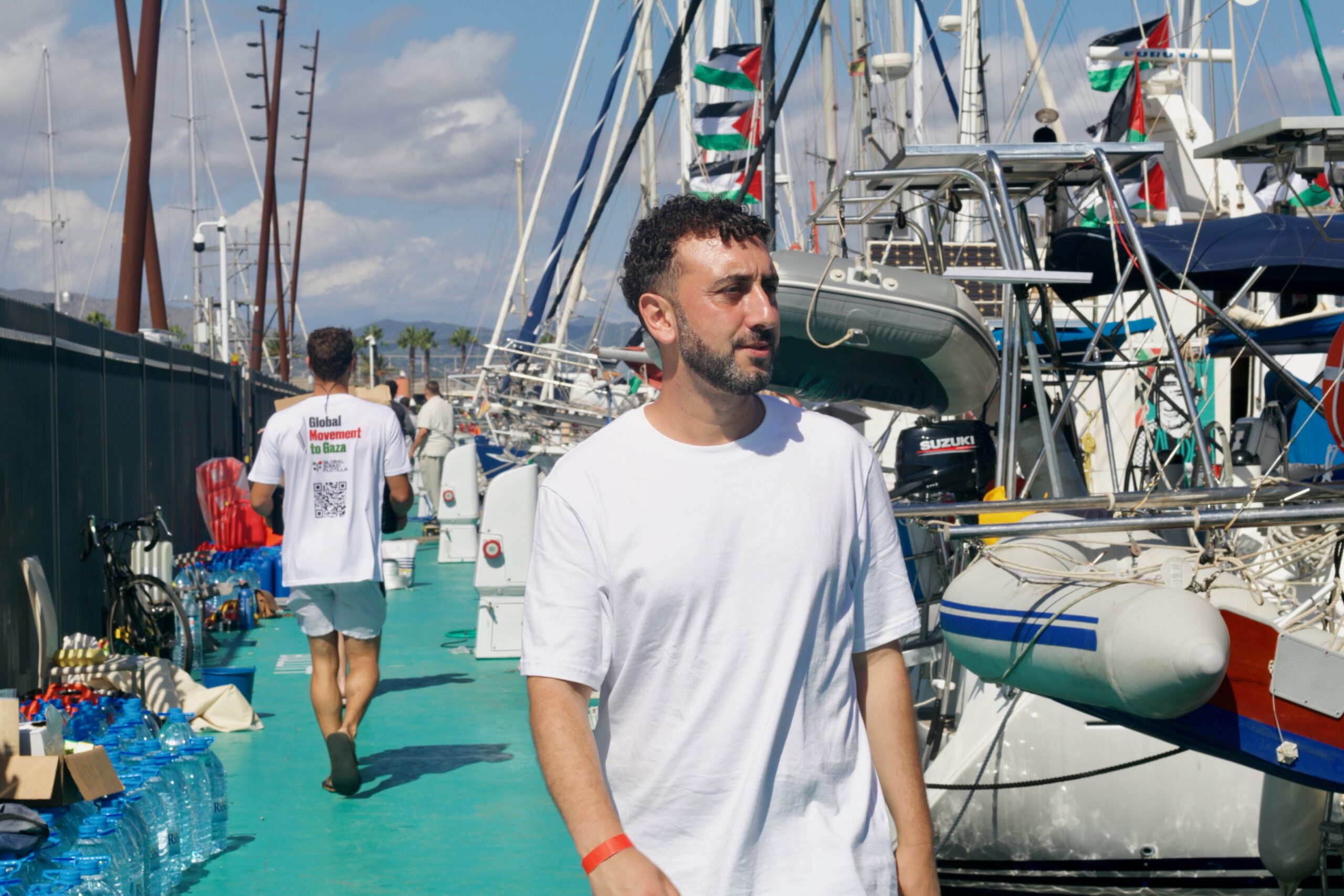 Kieran Andrieu walks down a pier past boats flying Palestine flags.