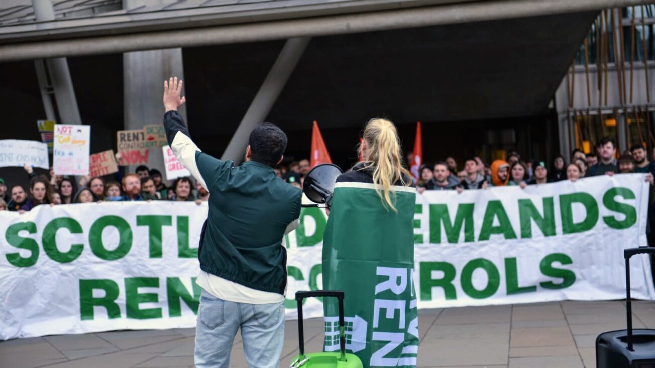People speak to a protest in front of a banner that says 'Scotland demands rent controls'