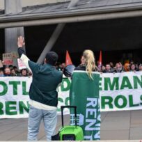 People speak to a protest in front of a banner that says 'Scotland demands rent controls'