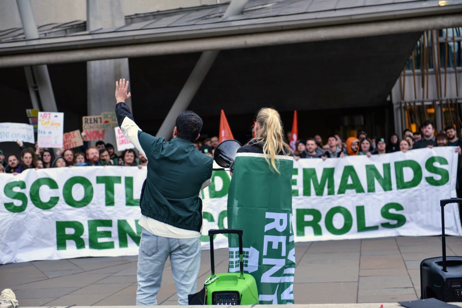 People speak to a protest in front of a banner that says 'Scotland demands rent controls'