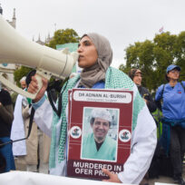 CAPTION: A protester holds a picture of Palestinian doctor Adnan Al-Bursh, who died in an Israeli prison, and chants slogans through a megaphone during the demonstration in Parliament Square. SOPA Images / Reuters