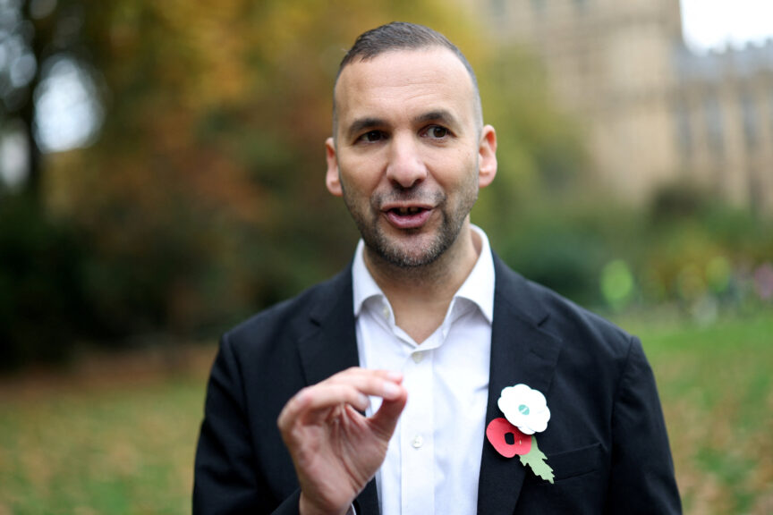 A man with short brown hair in a suit wears a red and white poppy together