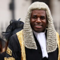 A man in a wig and black and gold velvet coat smiles