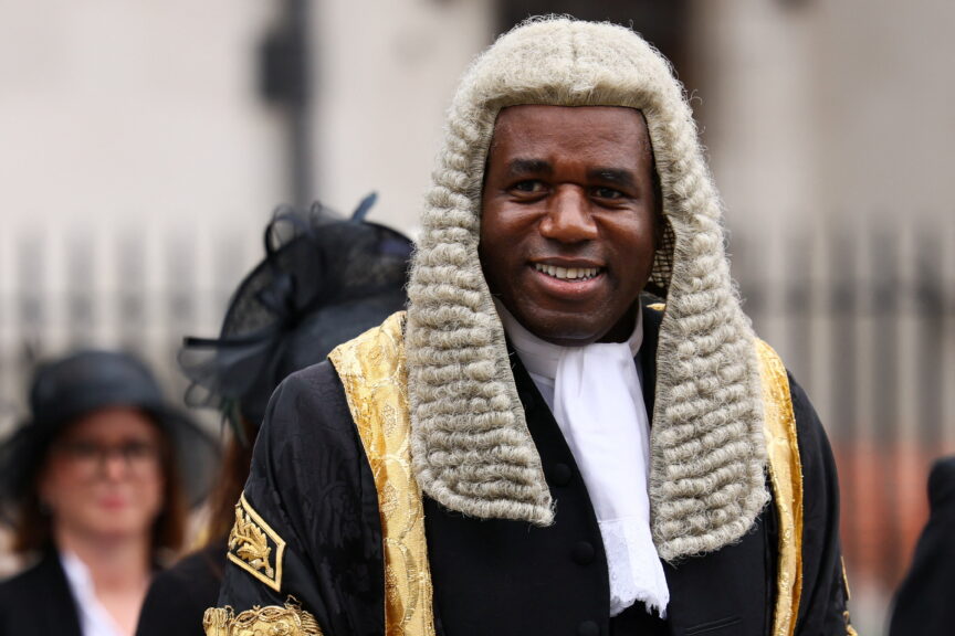 A man in a wig and black and gold velvet coat smiles