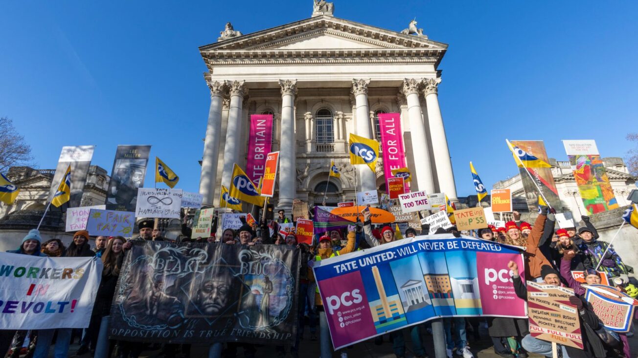A group of people hold placards outside of a neo-classical building