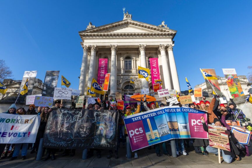 A group of people hold placards outside of a neo-classical building