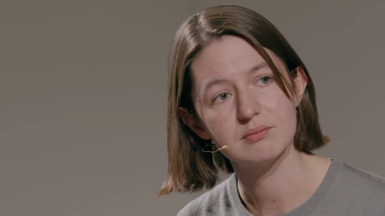 A woman with a brown bob and a face-adhesive microphone looks askance