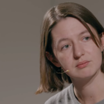 A woman with a brown bob and a face-adhesive microphone looks askance
