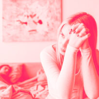 A woman looks into the distance as a man lies in bed topless