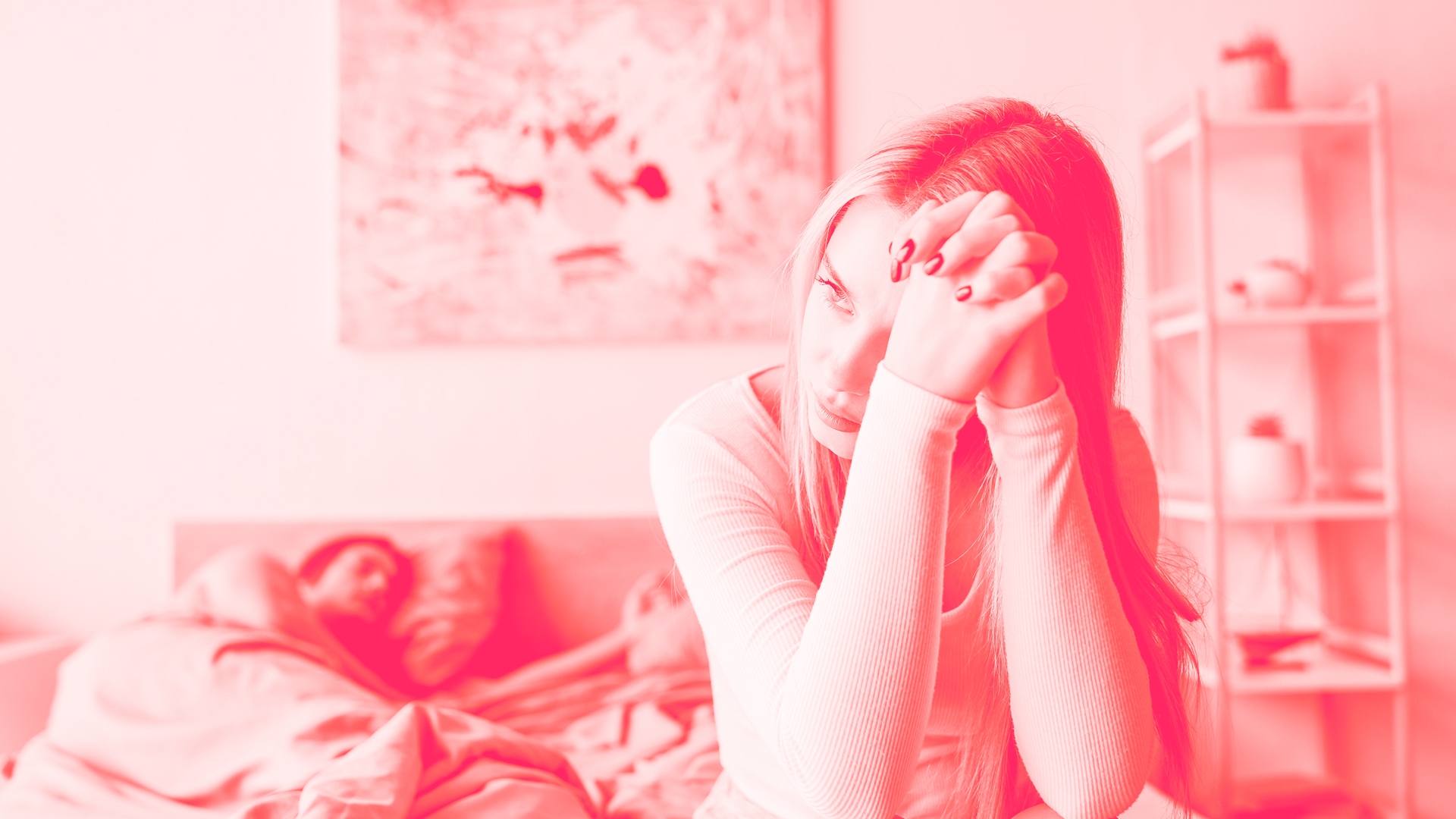 A woman looks into the distance as a man lies in bed topless