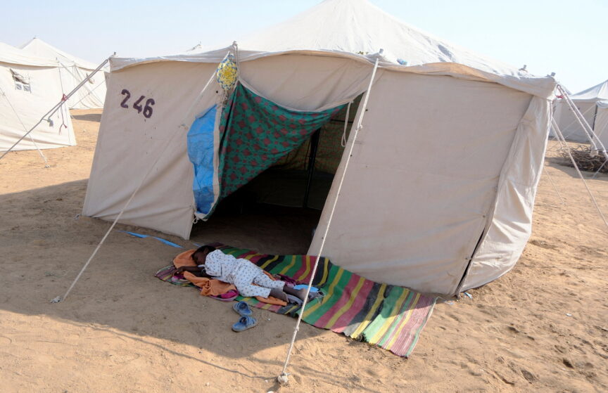 A child from El Fasher sleeps on the dusty ground outside a tent.